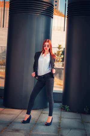 Fashion redhead young woman in sunglasses walking outdoor on streetの写真素材