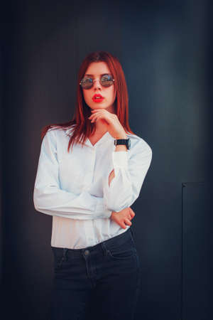 Fashion redhead young woman in sunglasses walking outdoor on streetの写真素材