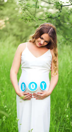 Pregnant woman in a white dress in a summer park