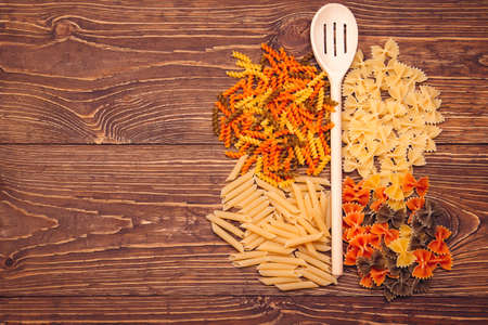 Different types of pasta,  lying around a wooden spoon on retro wooden background.  with copyspaceの写真素材