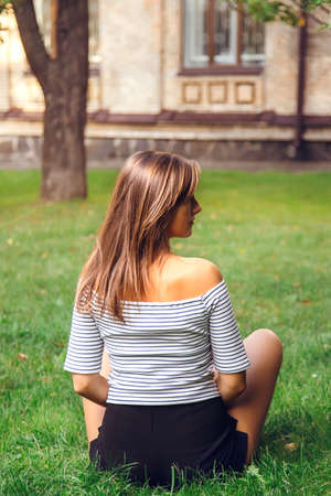 young beautiful happy woman sitting on the grass in the parkの写真素材