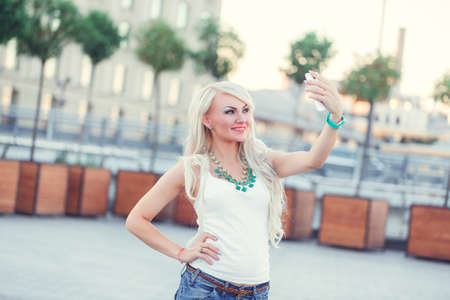 cheerful young woman walking and makes selfie on smartphone outdoorの写真素材
