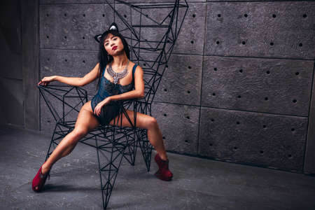 Beautiful slim model woman in underwear and cat ears on a posing with chair in studio.