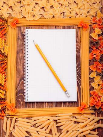 Pencil lying on a book of recipes frame of pasta on a wooden retro backgroundの写真素材