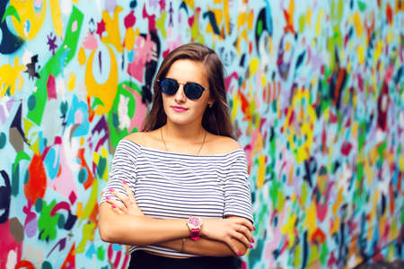 cheerful young woman with round glasses posing on the background of bright wallsの写真素材