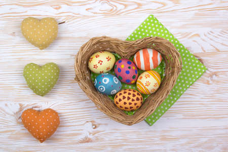 Colorful painted easter eggs in basket on light wooden backgroundの写真素材