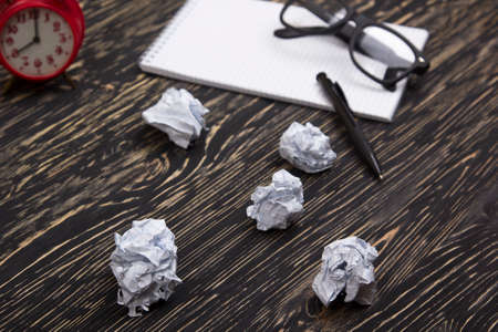 Crumpled paper balls with eye glasses and notebook on wood deskの写真素材