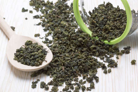 Spoon of dried green tea leaves on wooden background
