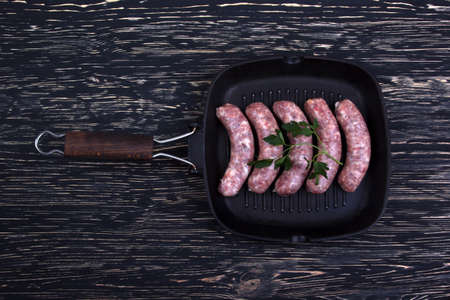 raw beef sausages on a cast-iron pan with rosemary and spices on a wooden table, South African boereworsの写真素材