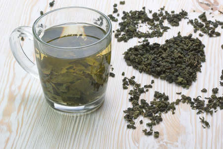 Green tea leaf in shape heart  on white wooden  background