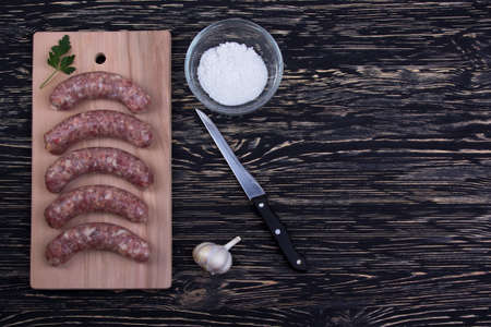 Raw sausages, garlic and knife on the cutting board.