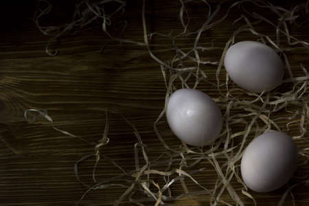 three eggs in the hay on a dark  wooden backgroundの写真素材