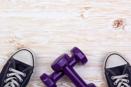 Fitness and sport equipment :sneakers and dumbbells with wooden background on top view