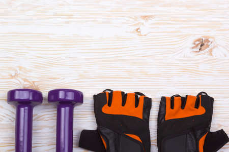 dumbbell and fitness gloves on light wooden background