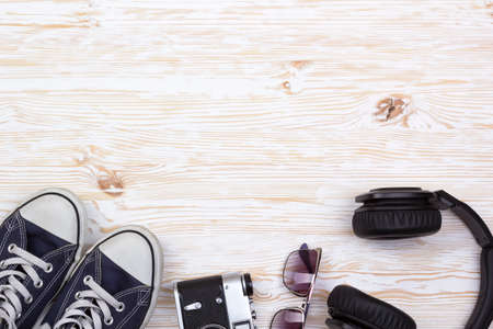Set of men's accessories: sneakers, camera, sunglasses and headphones on wooden background.