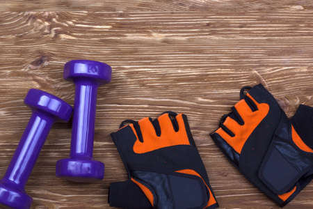 dumbbell and fitness gloves on brown wooden background