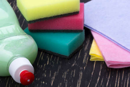 sponges, rsgs and a bottle of detergent on wooden background