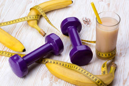 bananas, juice, measurement tape and dumbbells on wooden tableの写真素材