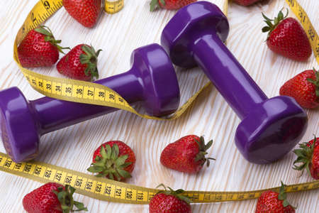 Strawberries, measurement tape and dumbbells on wooden tableの写真素材