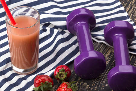 Strawberries, juice and dumbbells on white wooden deskの写真素材