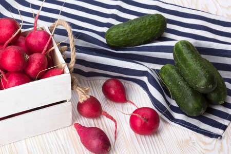 Cucumbers and red radishes in a wooden box on wooden desk