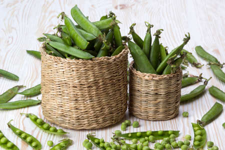 Fresh organic green peas in a basket on a wooden background.