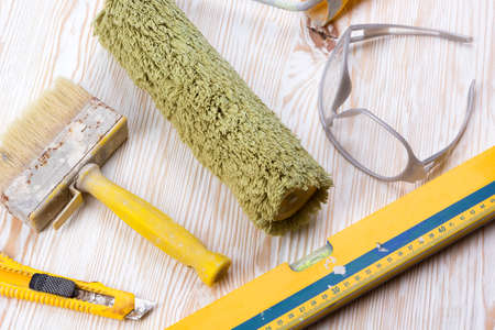 Construction tools: level, roller, glasses, knife and brush on wooden background