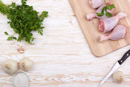 raw chicken drumstick on the board with salt, garlic, parsley on wooden tableの写真素材