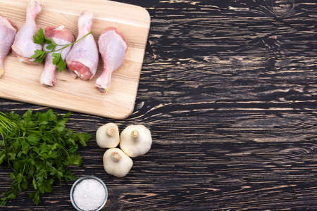 raw chicken drumstick on the board with salt, garlic, parsley on wooden tableの写真素材