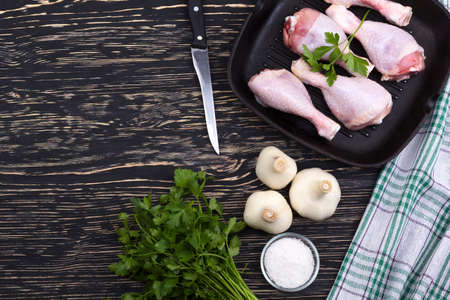raw chicken drumstick in pan with salt, garlic, parsley on wooden tableの写真素材