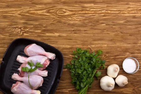 raw chicken drumstick in pan with salt, garlic, parsley on wooden tableの写真素材