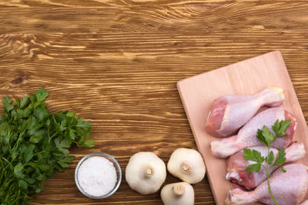 raw chicken drumstick on the board with salt, garlic, parsley on wooden tableの写真素材