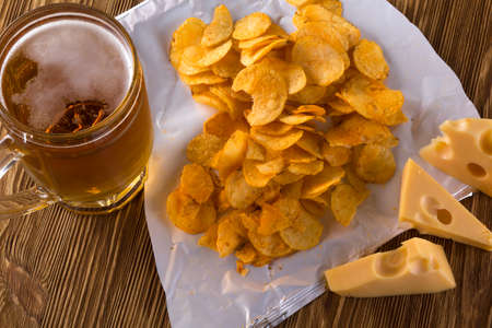 Potato chips, cheese and glass of beer on a wooden table.の写真素材