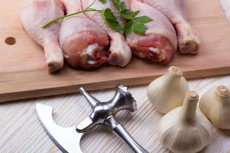 raw chicken drumstick on the board with salt, garlic, ax on wooden tableの写真素材