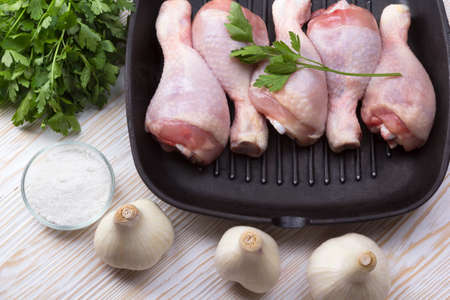 raw chicken drumstick in pan with salt, garlic, parsley on wooden tableの写真素材