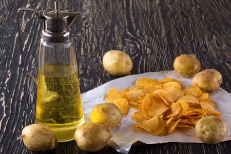 Potato chips, raw potato and jug of an oil on wooden background.の写真素材