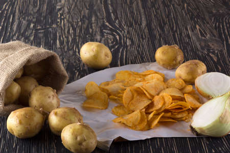 Potato chips, raw potato and onion on wooden background.の写真素材