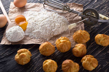 Tasty eclairs, eggs, flour and handle mixer on wooden background.の写真素材