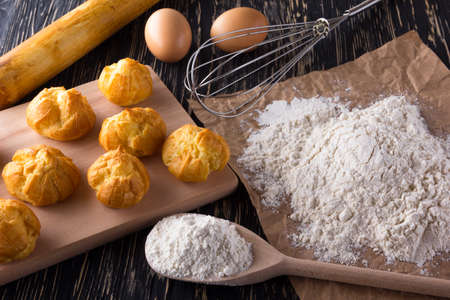 Tasty eclairs, eggs, flour and handle mixer on wooden background.の写真素材