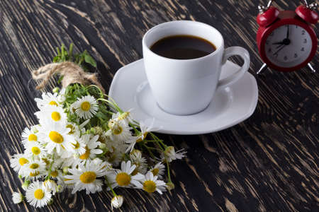 A cup of coffee,chamomile and alarm clock on wooden background.の写真素材