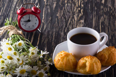 Eclair, coffee cup, alarm clock and charmomile on wooden background.の写真素材