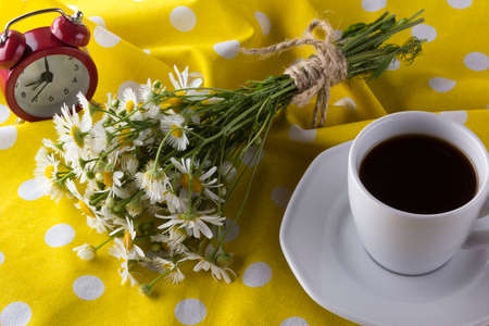 A cup of coffee,chamomile and alarm clock on wooden background.の写真素材