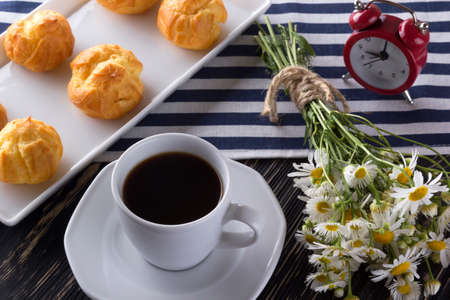 Eclair, coffee cup, alarm clock and charmomile on wooden background.の写真素材