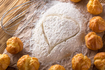 Heart of flour, eclairs and handle mixer on wooden background.