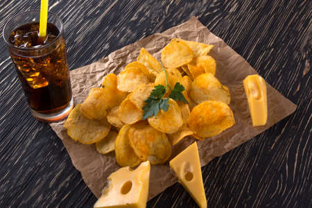 Potato chips, cheese with soda on wooden background