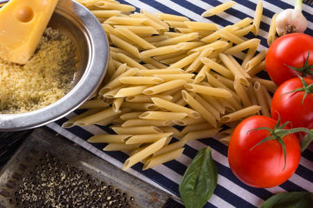 Pasta, tomatoes, garlic basil and grated cheese on wooden background.の写真素材