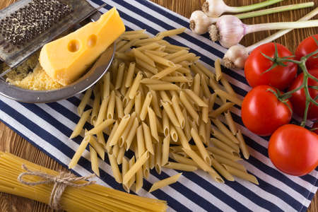 Pasta, tomatoes, garlic and grated cheese on wooden background.の写真素材