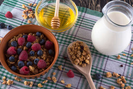 Muesli with fresh berries, honey, milk and alarm clock on wooden background.の写真素材
