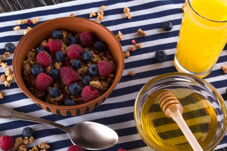 Muesli with fresh berries, honey and orange juice on wooden background.の写真素材