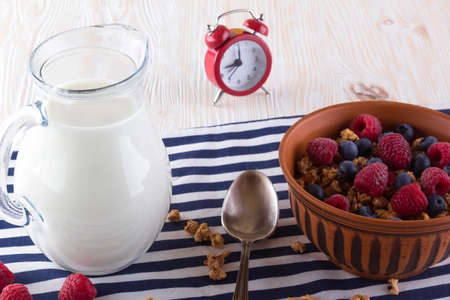 Muesli with fresh berries, milk and alarm clock on wooden background.の写真素材